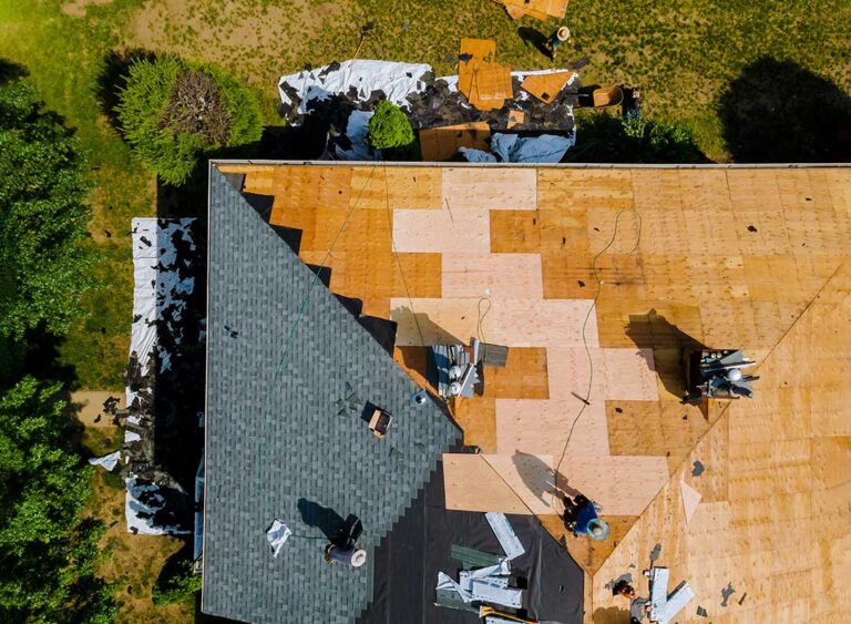 Homeowner clearing leaves from house gutters on a ladder in early spring.