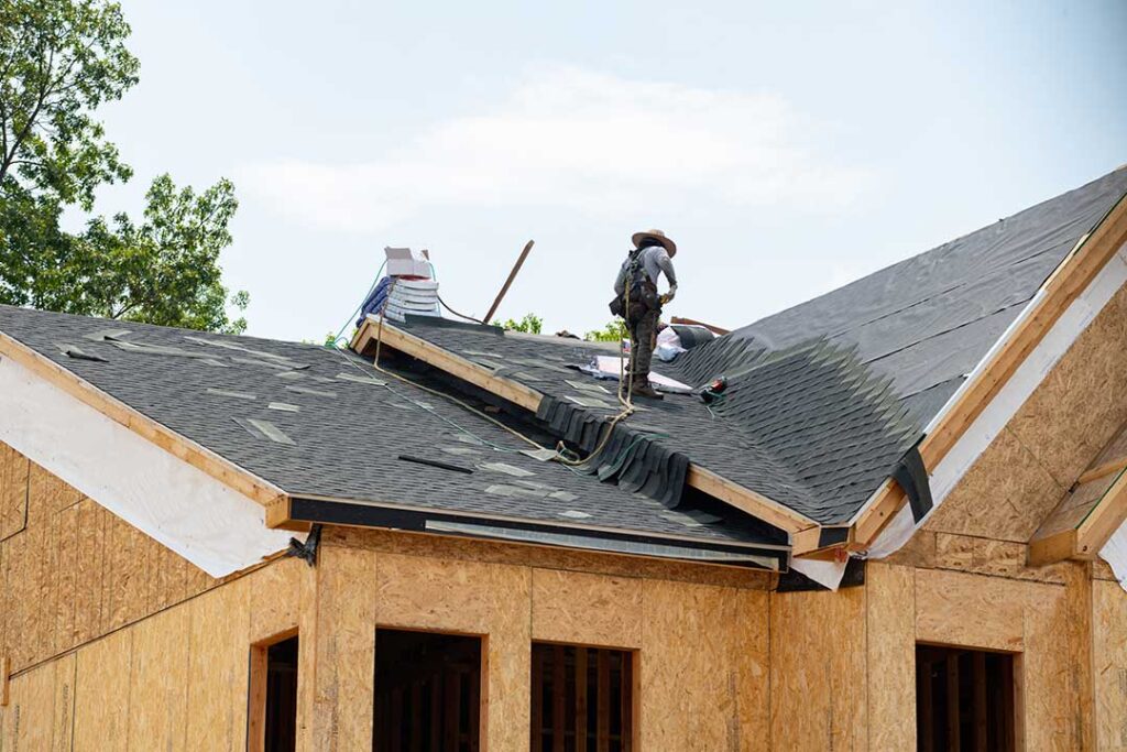Snow-covered roof with missing shingles, damp attic insulation, and a ceiling water stain inside a home.