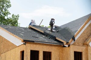 Snow-covered roof with missing shingles, damp attic insulation, and a ceiling water stain inside a home.